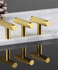 Set of three gold knurled T-bar cabinet handles on marble surface, featuring slick texture and modern design, reflection visible.