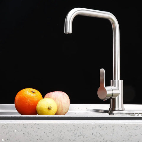 Stainless steel kitchen faucet with three fruits: orange, lemon, and apple resting on a countertop.