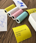 Four rolls of colorful square thermal receipt paper 57x25 mm for Mini POS printers on a wooden table.