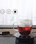 Fast Acting USB Mug Warmer With Smart Adjustable Heat Control Keeps Your Morning Sip Piping Hot All Day Long Sleek Black Tempered Glass Platform with glass cup of tea.