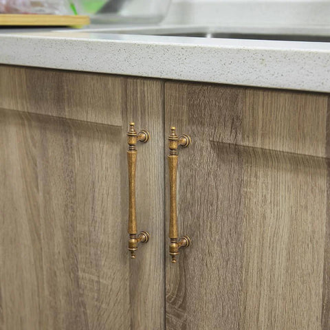 Six Pack 5 Inch Antique Brass Cabinet Pulls With Ornate Tapered Handles Decorative Finials And Sculpted Detailing shown installed on wooden cabinets.