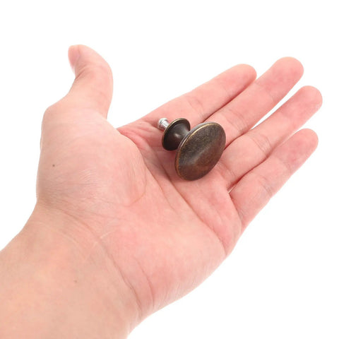 Person holding 12 Pack Round Antique Brass Cabinet Pulls Single Hole Small Flat Head Metal Drawer Handles for Kitchen and Bath Cabinets