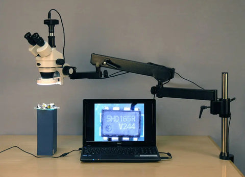 Pro Grade 3.5X-90X Trinocular Zoom Stereo Microscope With Articulating Arm And Pillar Clamp, 144 LED Illumination, Long Working Distance For Inspecting Circuit Boards, Dental Appliances, Jewelry, And Small Parts. Trinocular microscope on articulating arm over laptop and circuit board.