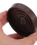 Person holding a brown foot pad from Four Pack Brown Rubber Furniture Foot Pads For Chair And Table Legs Non Slip Round Protectors Easy To Install Reduces Friction On Hardwood Floors Keeps Floors Quiet And Scratch Free.