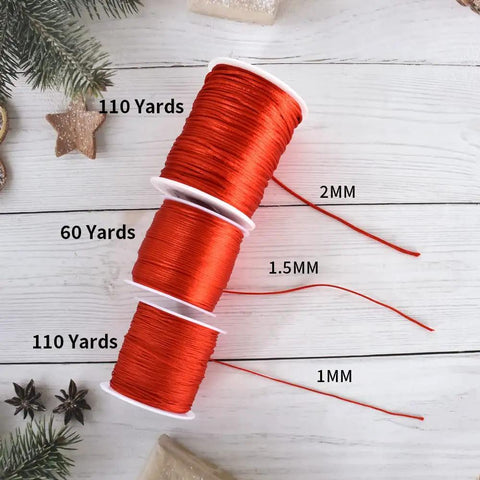 Three spools of red nylon satin cord in sizes 2mm, 1.5mm, and 1mm on a white wooden background with holiday decor