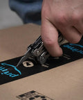 Close-up of hand using the 13 In 1 Stainless Steel EDC Multitool with knife blade to cut through packaging tape on a cardboard box.
