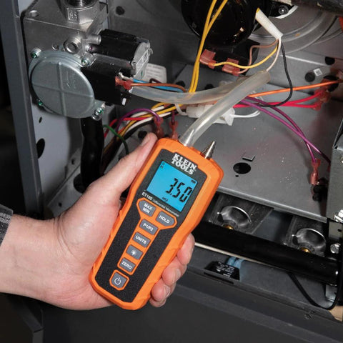 Klein Tools ET180 digital manometer with orange housing, handheld air pressure tester near wiring and tubing.