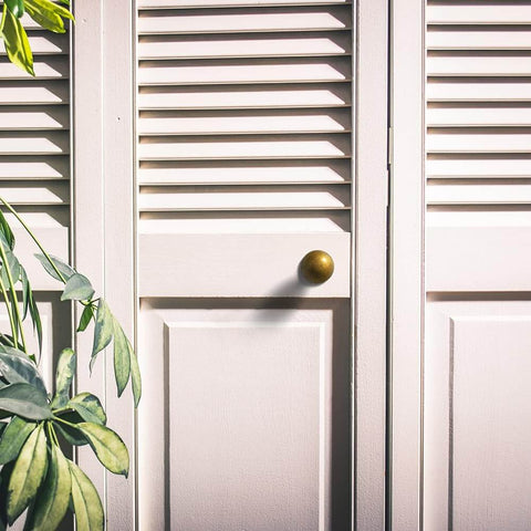 Set Of Twelve Sleek Round Antique Brass Cabinet Knobs For Rustic Modern Kitchens And Vintage Furniture Makeovers One And One Eighth Inch Diameter Durable Hardware For Cabinets Drawers And Dressers With Bold Rustic Charm installed on white louvered door