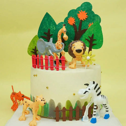 Jungle-themed cake with animal figurines, including an elephant, lion, giraffe, zebra, surrounded by red and brown picket fences.