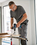Man using 18V Cordless Combi Drill with 150 Nm Torque Brushless Motor Pro Grade Power Tool on wood surface.