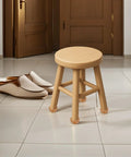 Round wooden stool on tiled floor, door, and slippers in the background