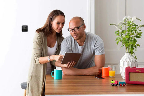 Couple using tablet with T5 Plus WiFi Touchscreen Smart Thermostat With 7 Day Flexible Programming Geofencing Technology Black on wall.