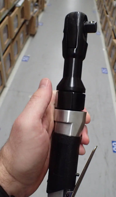 Close-up of Three Eighths Inch Pneumatic Ratchet Wrench Beefy Heavy Duty Tool For Auto Shop Seventy Foot Pounds Of Torque One Hundred Sixty RPM Ninety PSI Three Hundred Sixty Degree Swivel Joint Narrow Space Design Easy Left Right Switch Quick Sleeve Change held in hand, showing the black and silver components.