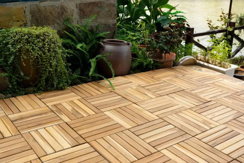 Outdoor patio with 12x12 Inch Solid Wood Interlocking Flooring Tiles Pack Of 9 in Real Acacia Hardwood, surrounded by plants.