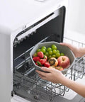 Portable Countertop Dishwasher Fully Automatic Compact Kitchen Essential With Intelligent Air Dry and Spacious Rollout Basket For Tiny Homes Ditch The Sink Grime Quick Cleanup Perfection, loading fruit into the basket.