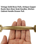 Hand holding vintage solid brass pull in antique copper finish, rustic barn door handle for cabinets and drawers, 6.5 inch length.