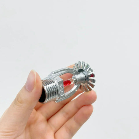 Top Notch Two Pack Fire Sprinkler Heads With Automatic One Fifty Five Degree Fahrenheit Activation For Serious Safety Needs Built Tough For Any Building In A Simple Pendant Down Spray Mount That Handles Extreme Heat Without Breaking A Sweat, showing a hand holding a silver brass sprinkler head with red sensor.