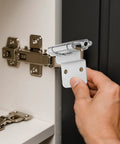 Close-up of a silver metal self-closing inset cabinet hinge being installed on a kitchen cabinet door
