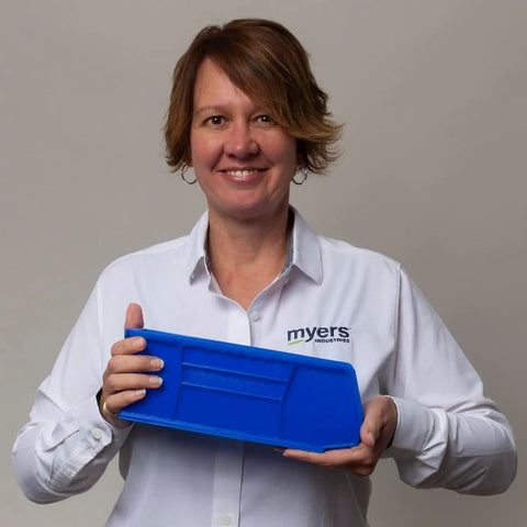 Person holding a blue plastic storage bin lid, wearing a white shirt with company logo.