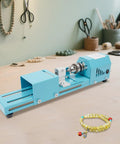 This Badass Mini Wood Lathe Is The Ultimate Desktop Turnin' Tool For Your DIY Crafts on a workbench with beads.