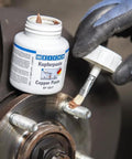 Front view of WEICON Copper Paste bottle (4.2 oz) with brush applying copper anti-seize to a wheel hub stud