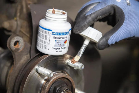 Front view of WEICON Copper Paste bottle (4.2 oz) with brush applying copper anti-seize to a wheel hub stud