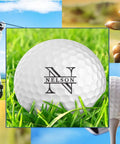 Focus on personalized golf ball with name and initials in grass, surrounded by a golfer and clubs, part of 12 pack custom monogram golf balls.