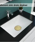 Gold Stainless Steel Shower Drain Catcher With Soft Silicone Edge Flat Round Tub Strainer in a white bathroom sink.
