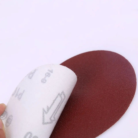 Get This Awesome 100 Piece 7 Inch Hook And Loop Sandpaper Disc Set With Grits From 60 To 1000 For Wet Or Dry Sanding Projects And Polishing That Gets The Job Done Smooth And Quick Every Single Time, showing a 7 inch red sandpaper disc being peeled.