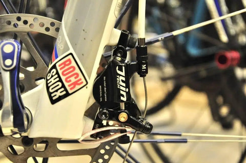 M1 Hybrid Hydraulic Disc Brake Caliper Set on silver RockShox fork, showing cable-actuated hydraulic system for enhanced braking.