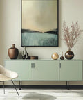 Modern living room with a minimalistic green cabinet featuring stainless steel handles and abstract artwork above, styled with decorative vases.