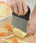 Crinkle cutter with black handle and stainless steel blades slicing a potato into crinkle-cut fries on a wooden board