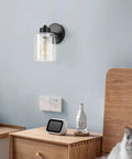 Matte Black Metal Wall Sconces With Clear Glass Shades Two Pack Modern Bathroom Vanity Lights Brushed Brass Finish Easy Mount Wall Light Fixtures For Bath And Hallway, shown mounted above a nightstand.