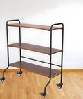 Three-shelf rolling cart with black metal frame and brown wood shelves on casters