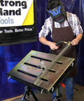 Person welding on worksite ready welding table pro grade with 1.1 inch slot top adjustable height and tilt casters.