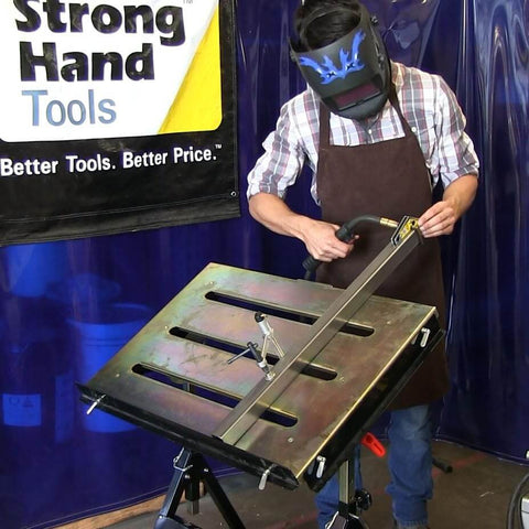 Person welding on worksite ready welding table pro grade with 1.1 inch slot top adjustable height and tilt casters.