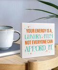 Your Energy Is a Luxury Inspirational Quote Wood Box Sign Desk Decor next to a coffee mug on a wooden table in a home office setting.