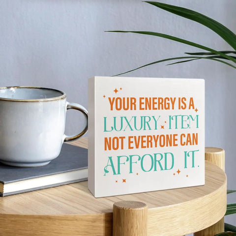 Your Energy Is a Luxury Inspirational Quote Wood Box Sign Desk Decor next to a coffee mug on a wooden table in a home office setting.