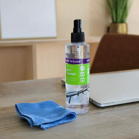 Front view of Flents Wipe 'N Clear lens cleaner spray bottle (8 oz) with blue microfiber cloth on desk.