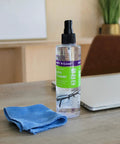 Front view of one Wipe'N Clear lens cleaner spray bottle and blue microfiber cloth on a wooden desk