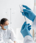 Sealed glass vial being drawn into a syringe by blue-gloved hands in a clinical setting.
