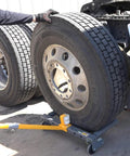 WinnTec rolling wheel dolly under a large truck tire; orange arm, gray base, side view