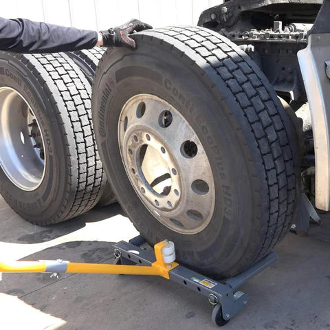 WinnTec rolling wheel dolly under a large truck tire; orange arm, gray base, side view