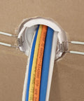 White 2-inch cable pass-through port, pair, installed in drywall with blue and orange cables.