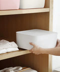 Person placing Stackable White Plastic Drawer Organizers for Bras Socks and Underwear on a wooden shelf with clothes underneath.