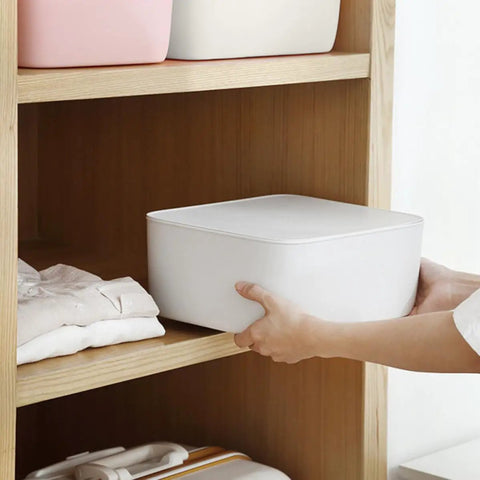 Person placing Stackable White Plastic Drawer Organizers for Bras Socks and Underwear on a wooden shelf with clothes underneath.