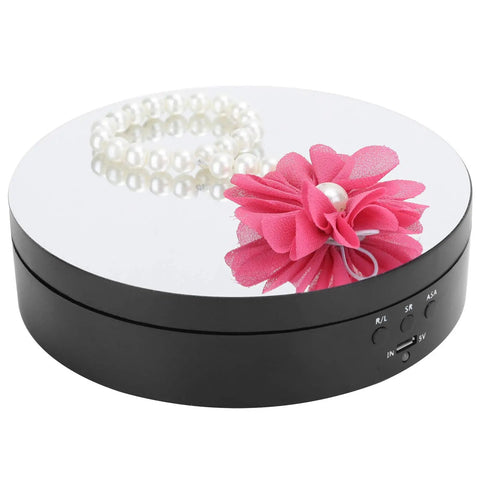 Spiffy Omquot Electric Rotating Jewelry Stand With 360 Degree Swivel Plate And Usb Charging Port For Watches Cosmetics And Toys In Sleek Black Finish with pearl bracelet and pink flower on mirror surface.