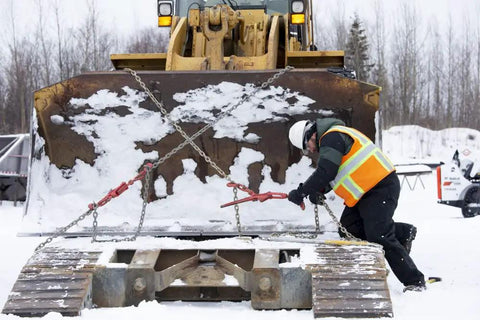 Worker in winter gear outdoors adjusting chains on machinery, highlighting durable use for Winter Work Gloves With Waterproof Barrier And 100g PrimaLoft Gold Insulation Touchscreen Compatible Black And Gray X Large Built For Moderate Cold Weather Grip Ready Durable All Day Comfort For Tough Job Sites.