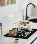 Spooktacular Black Witches Brew Coffee Station Mat Featuring Quick Dry Absorbent PU Material Designed For Kitchen Counter Espresso Machine Setup 28 By 18 Inch Halloween Spill Proof Drip Catch Pad on modern kitchen counter.