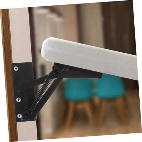 Front view of black folding lifting hinge with coil spring mounted to a wooden door frame, supporting a white padded panel.
